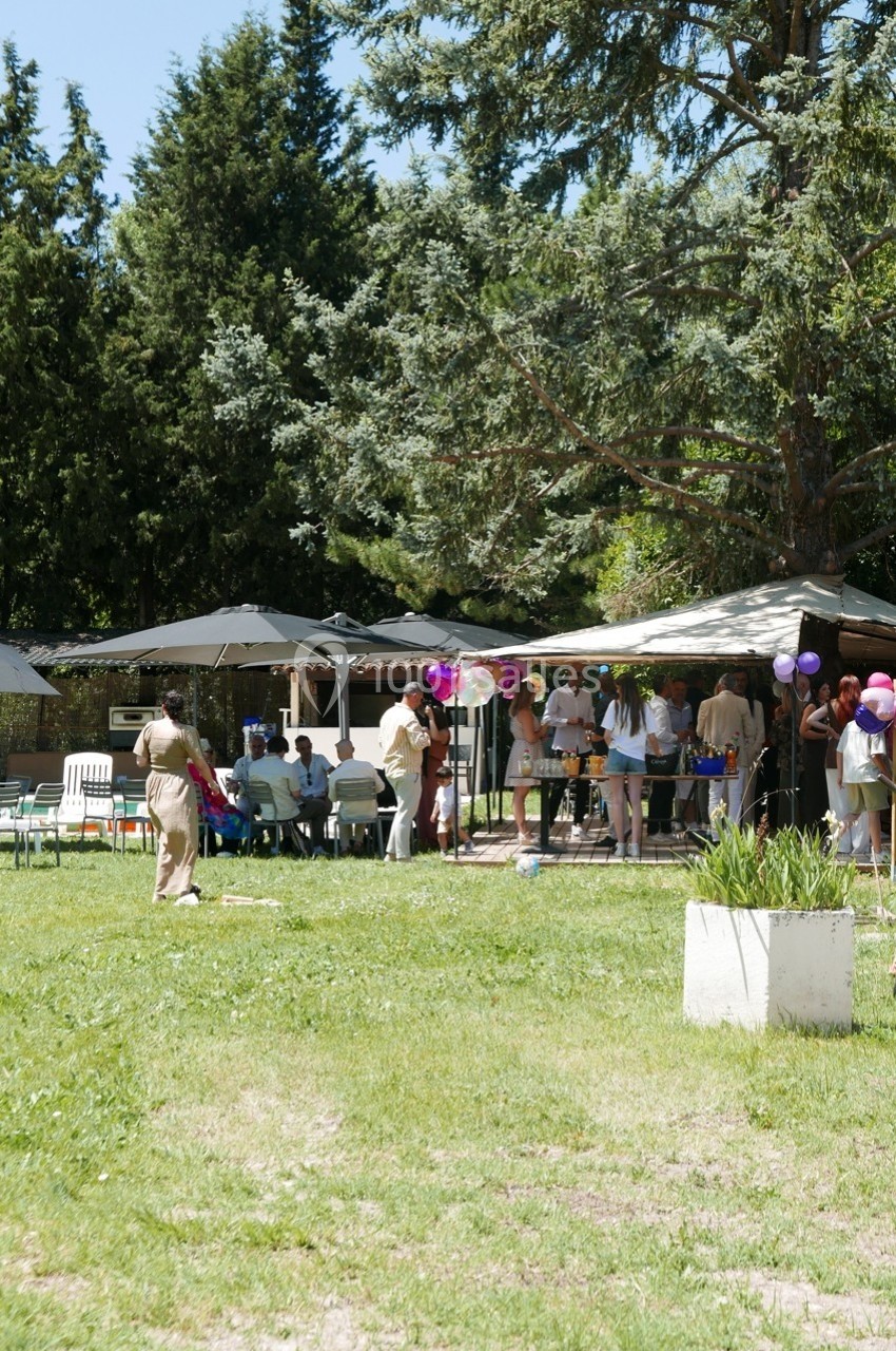 Groupe de personnes rassemblées dans un jardin, près de tables et parasols, entourées d'arbres et de verdure.