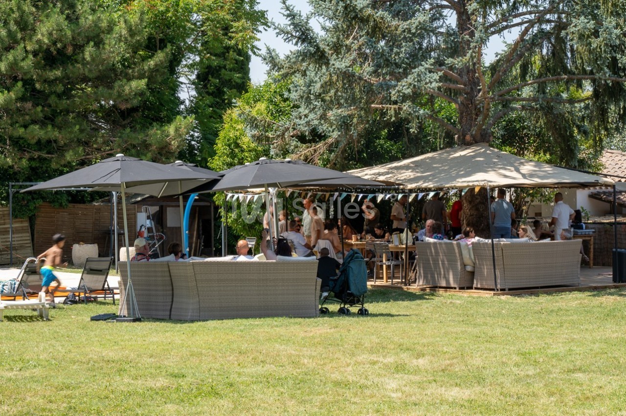 Groupe de personnes réunies dans un jardin avec des parasols, des canapés et une piscine en arrière-plan.