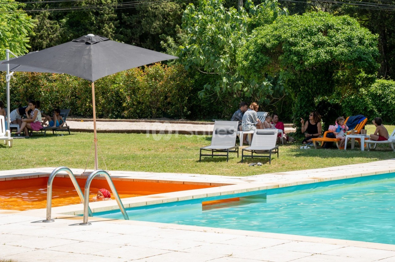 Des personnes assises sur des chaises longues et à l'ombre près d'une piscine entourée de verdure.