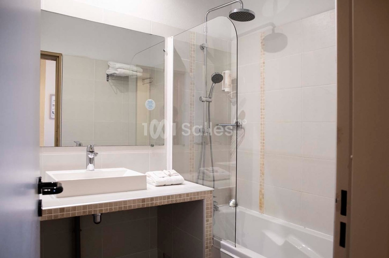 Salle de bain moderne avec lavabo, miroir, baignoire équipée d'une paroi vitrée et douchette murale.