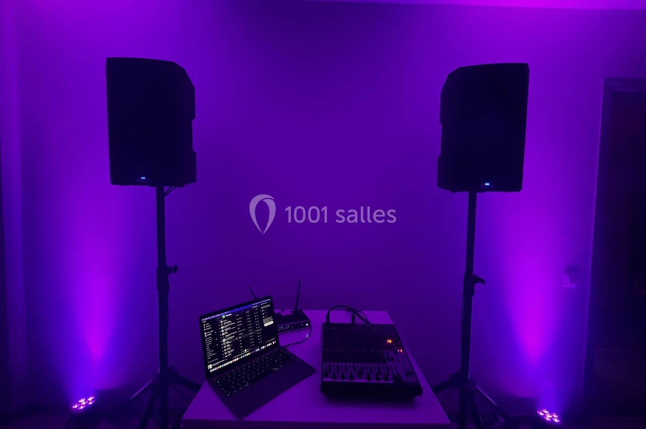 Deux enceintes sur pieds entourent une table avec un ordinateur portable et une console audio, éclairées par une lumière…