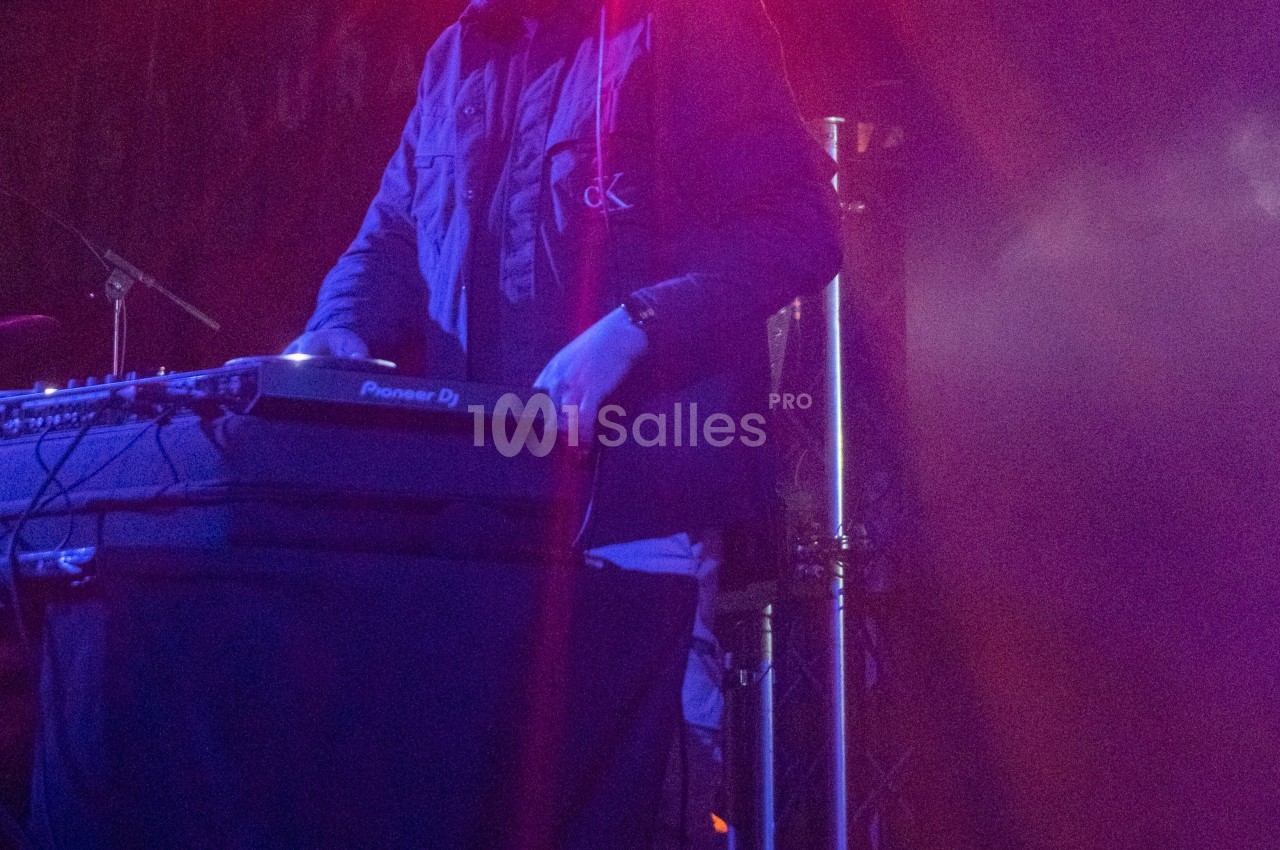 Un DJ mixant sur une table de mixage, éclairé par des lumières violettes dans une ambiance de concert.