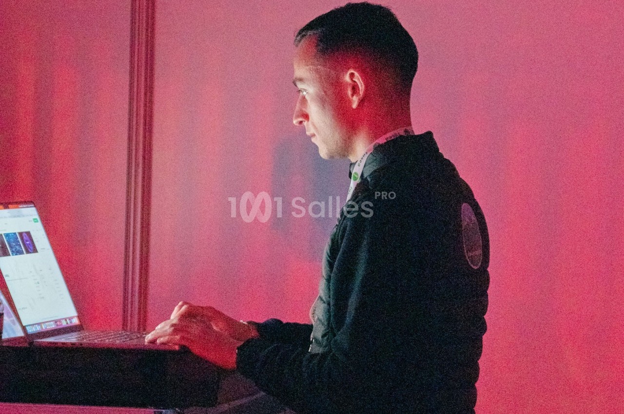Un homme utilise un ordinateur portable dans un environnement éclairé par une lumière rouge.