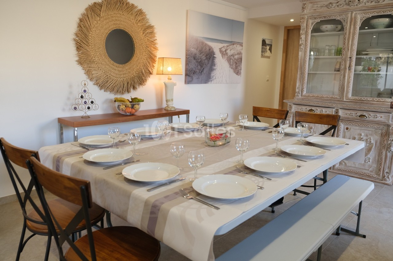 Table dressée pour un repas, avec assiettes, verres et couverts, dans une salle à manger lumineuse et décorée.