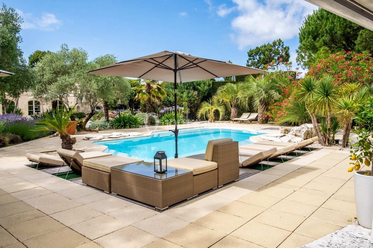Piscine extérieure entourée de transats, parasols et végétation luxuriante dans un cadre ensoleillé.