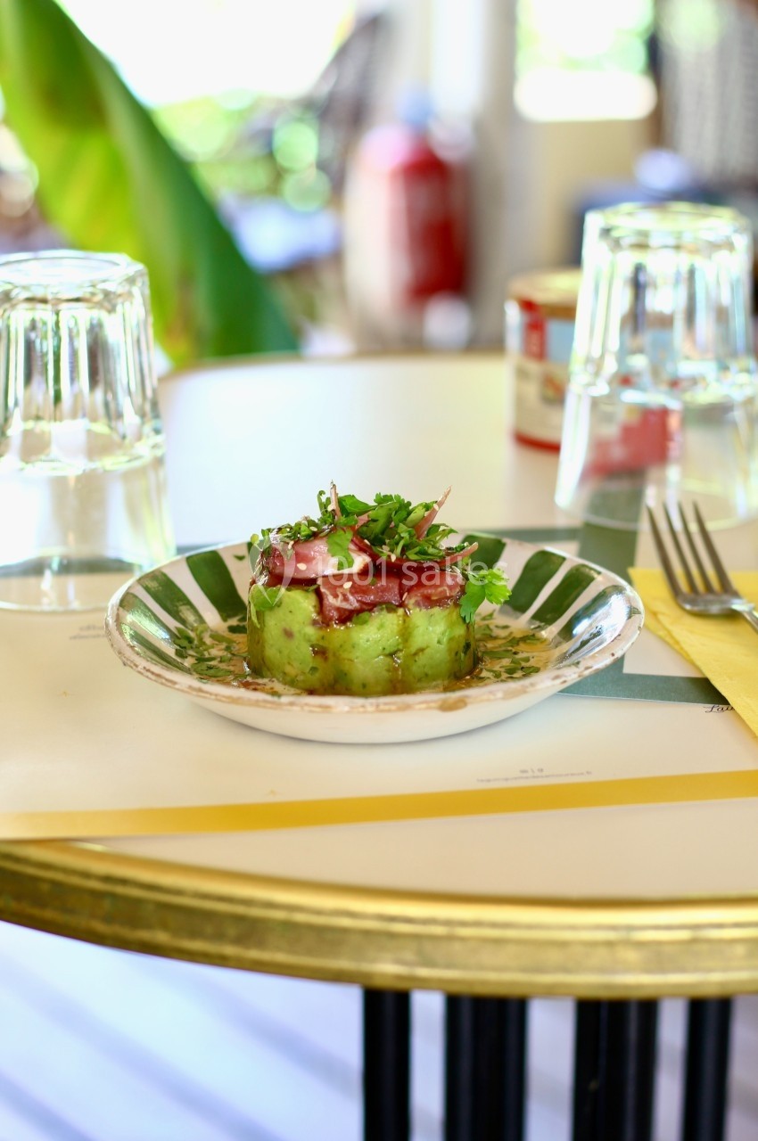 Plat de tartare d'avocat et poisson cru, garni de fines herbes, servi sur une assiette en céramique sur une table dressée.