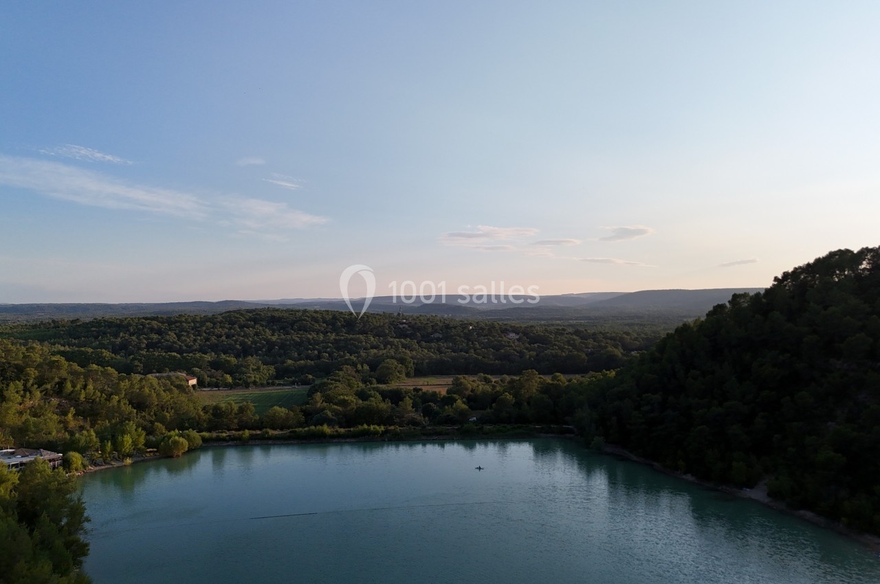 Vue aérienne d'un lac entouré de collines boisées sous un ciel dégagé au coucher du soleil.