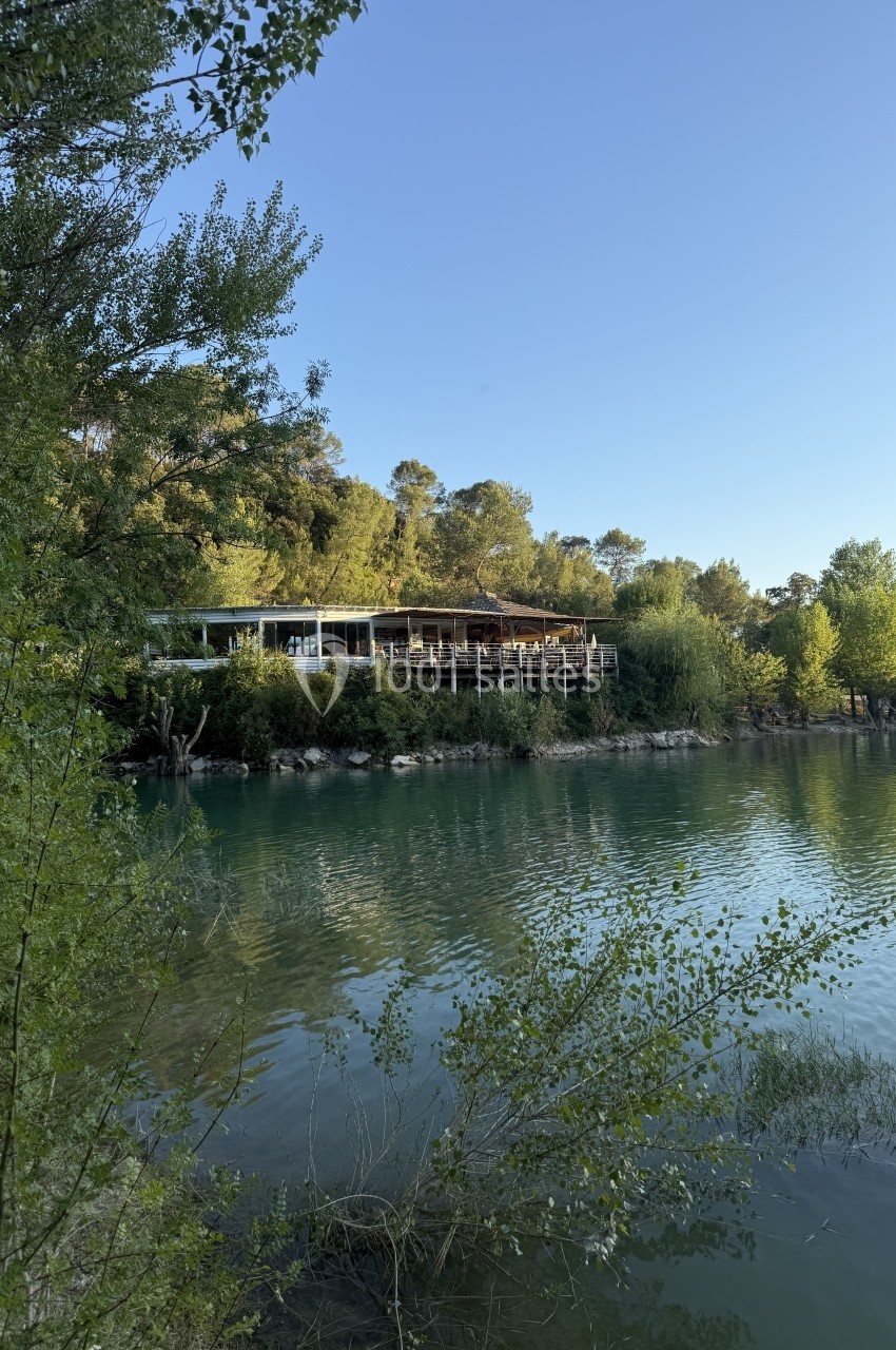 Bâtiment en bois au bord d'une rivière entourée de végétation, sous un ciel dégagé en fin de journée.