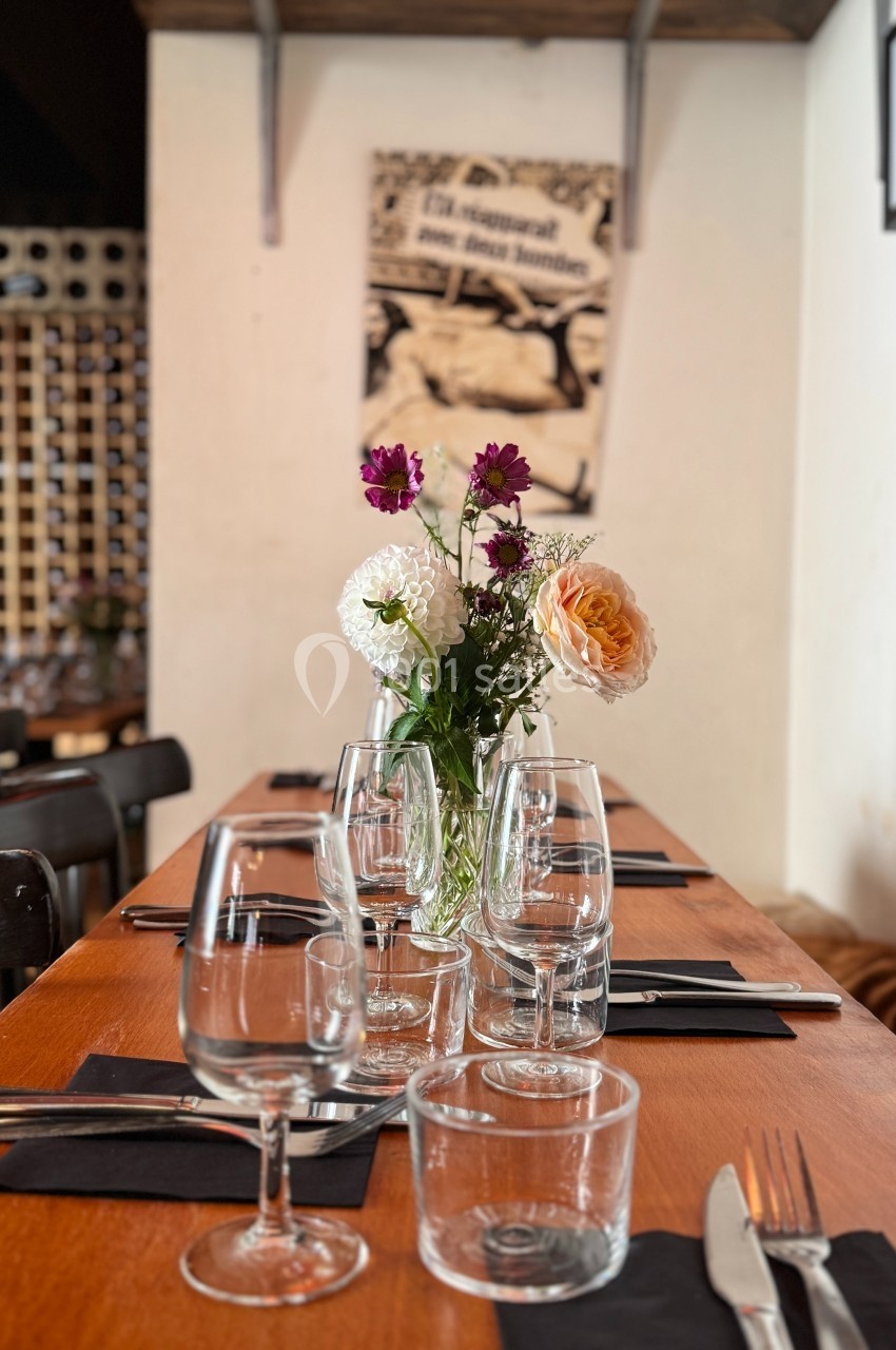 Table dressée avec des verres, couverts et un vase de fleurs, dans un restaurant à l'ambiance chaleureuse.