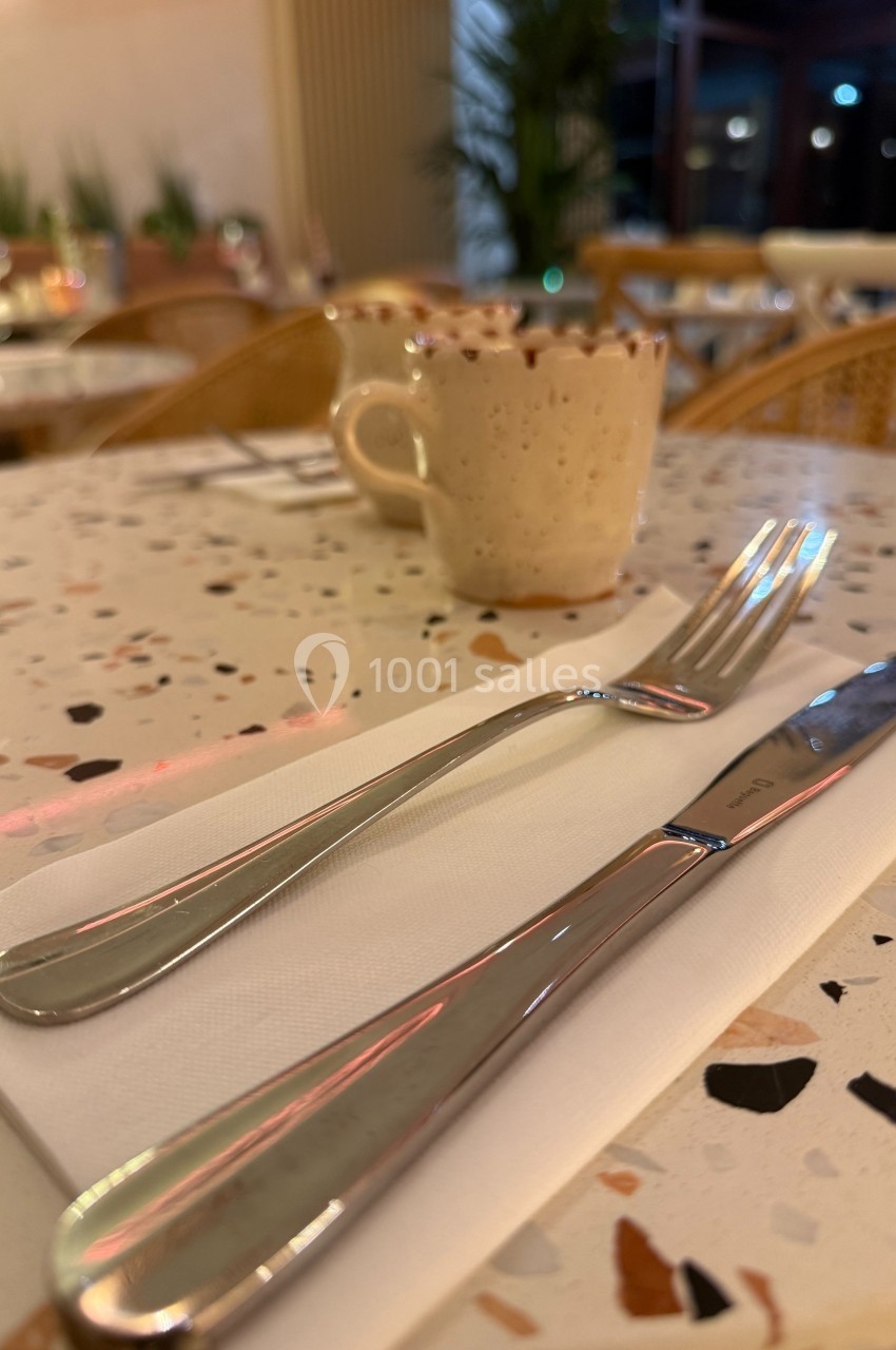 Couverts en métal posés sur une serviette blanche sur une table en terrazzo, avec une tasse en arrière-plan.