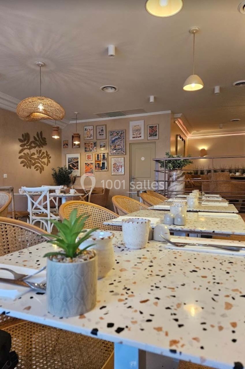 Salle de restaurant lumineuse avec tables en terrazzo, chaises en rotin et décoration murale colorée.