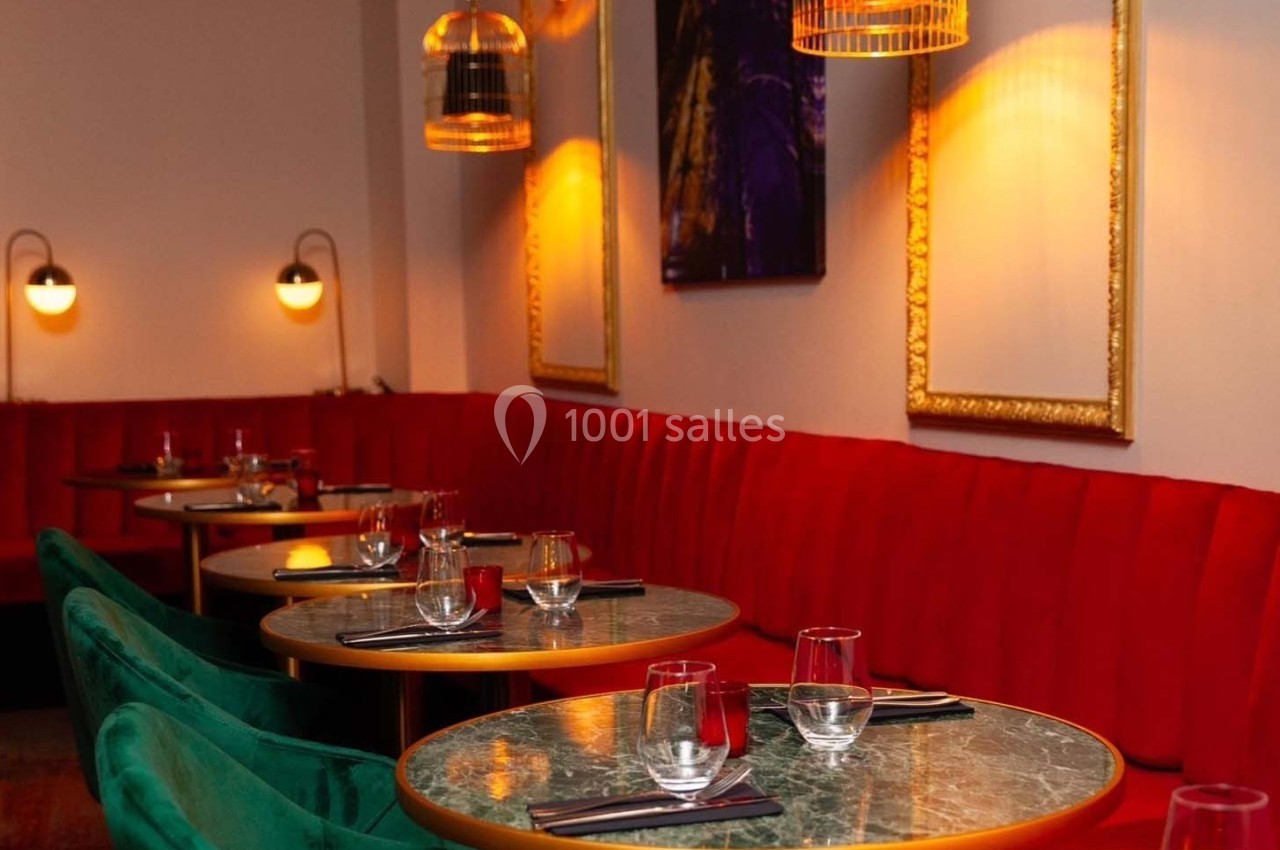 Salle de restaurant avec banquettes rouges, tables rondes en marbre vert, chaises vertes et éclairage tamisé.
