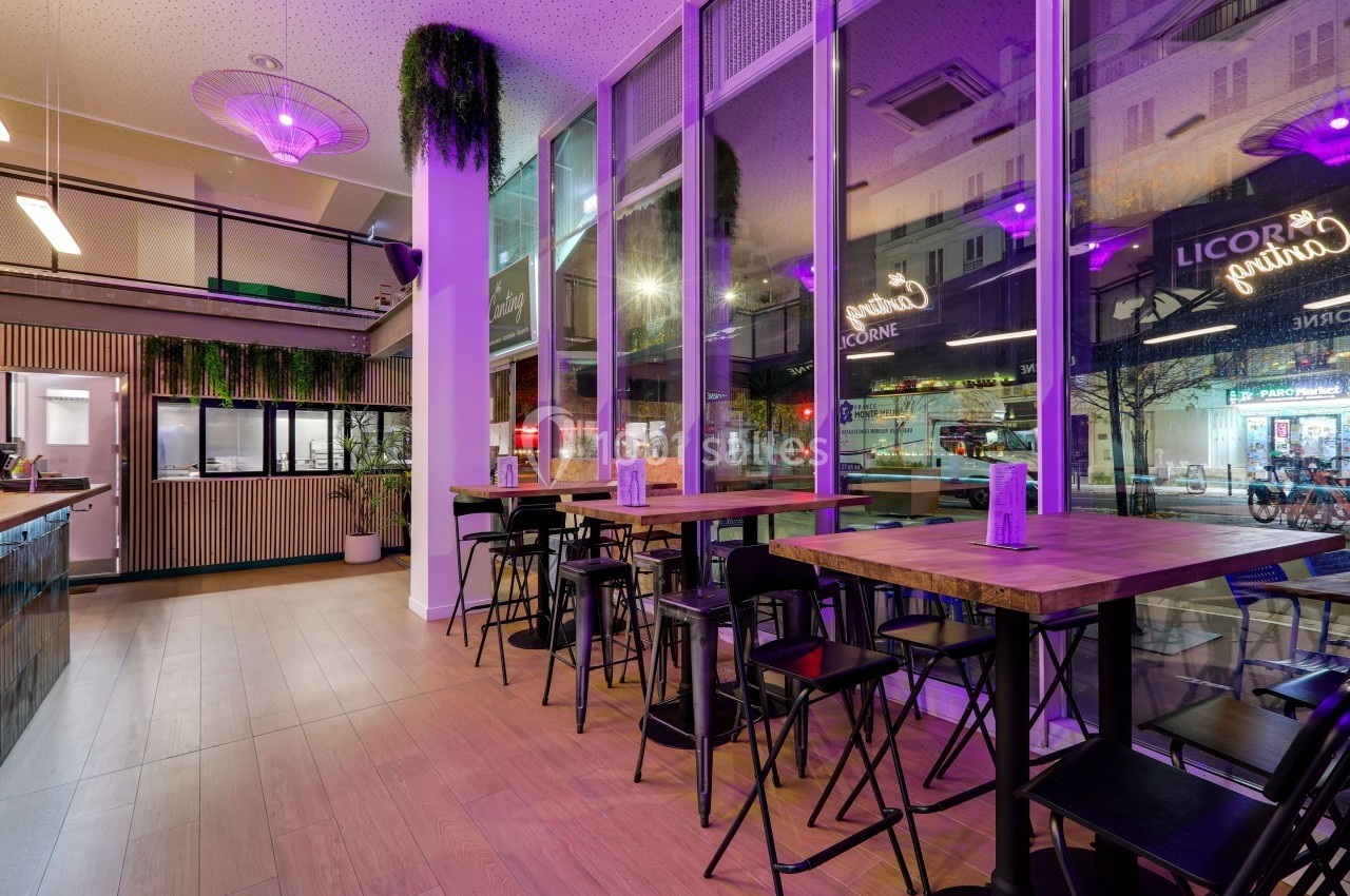 Salle de restaurant moderne avec grandes baies vitrées, éclairage violet et mobilier en bois et métal.