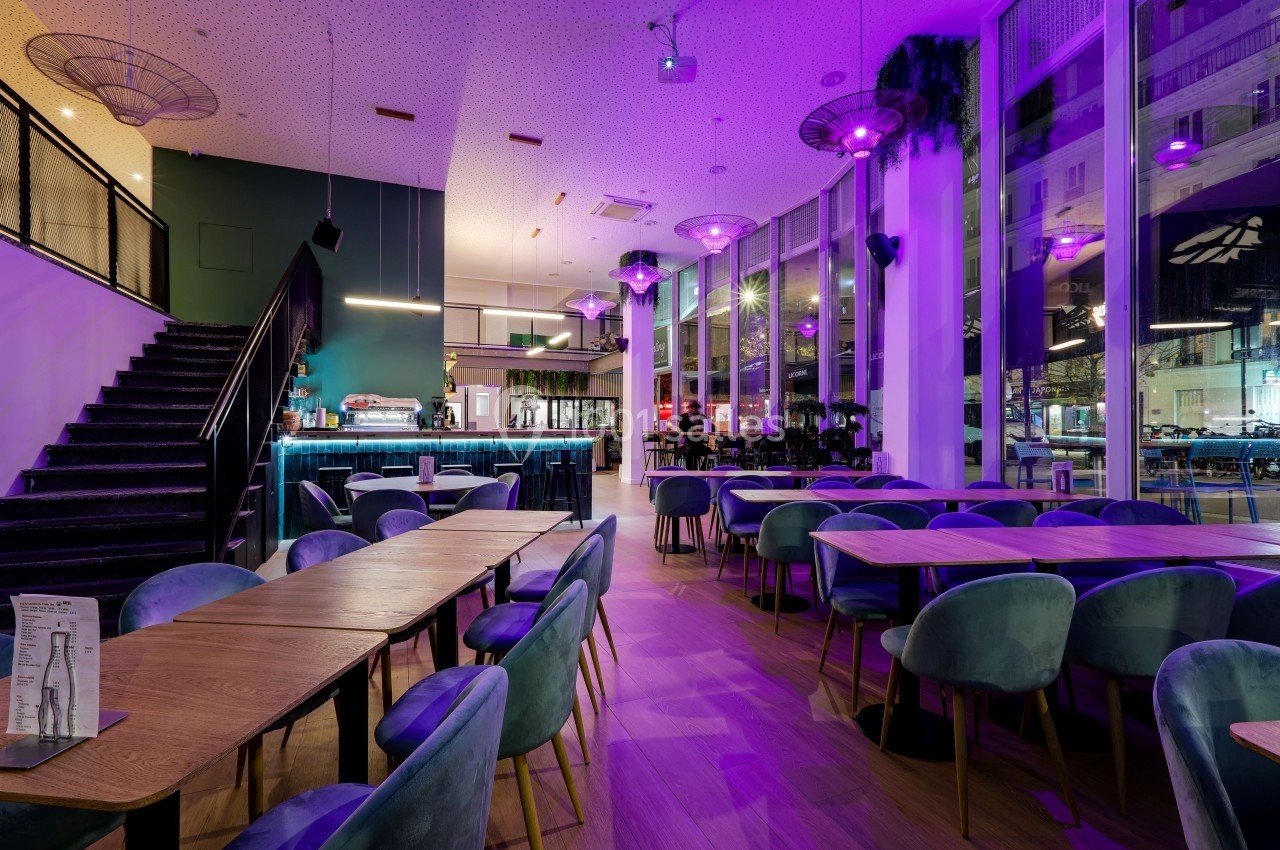Salle de restaurant moderne avec tables en bois, chaises colorées et éclairage violet, donnant sur de grandes baies vitrées.