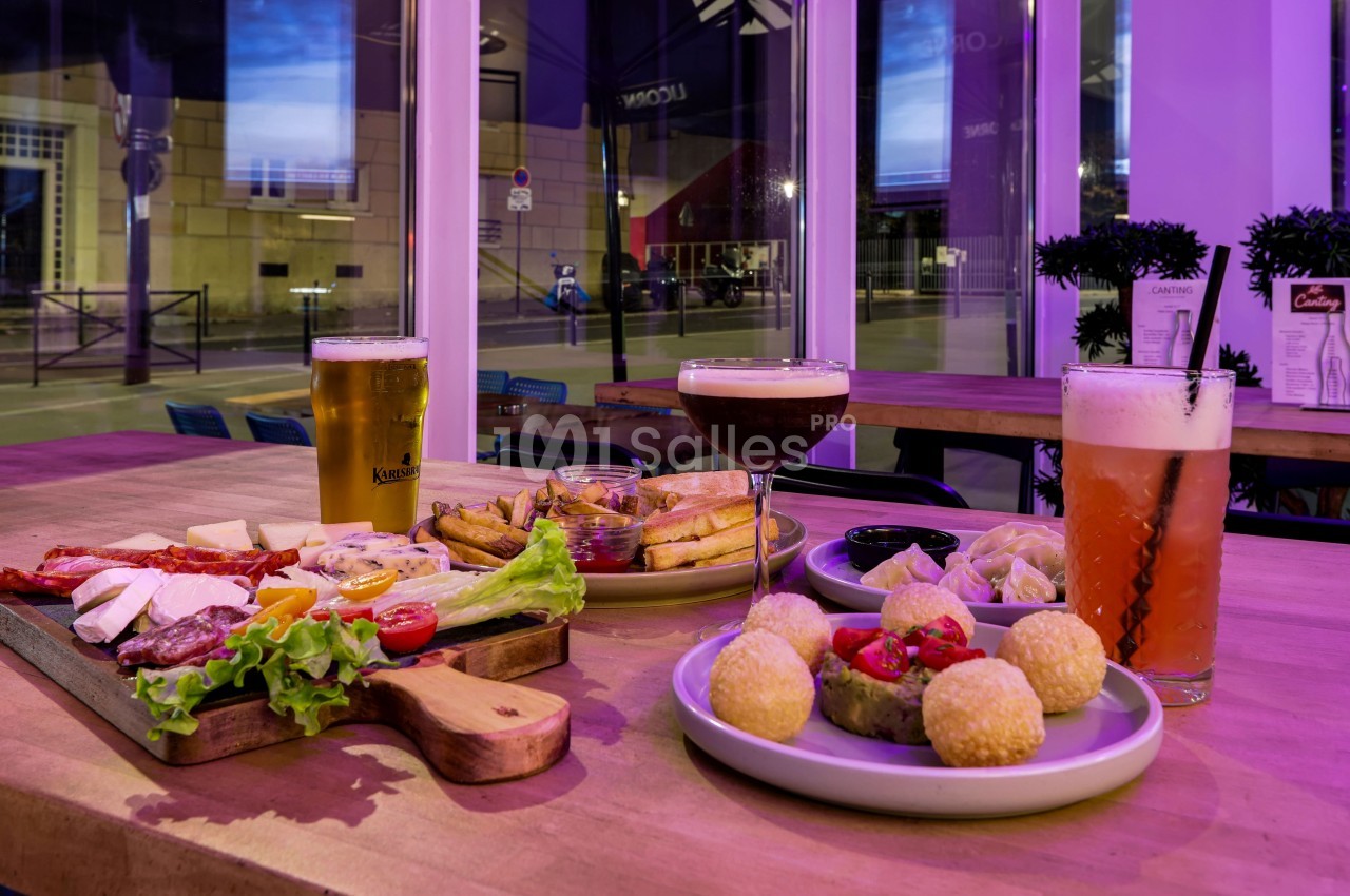 Assortiment de plats et boissons sur une table en bois dans un restaurant avec vue sur des fenêtres donnant sur la rue.