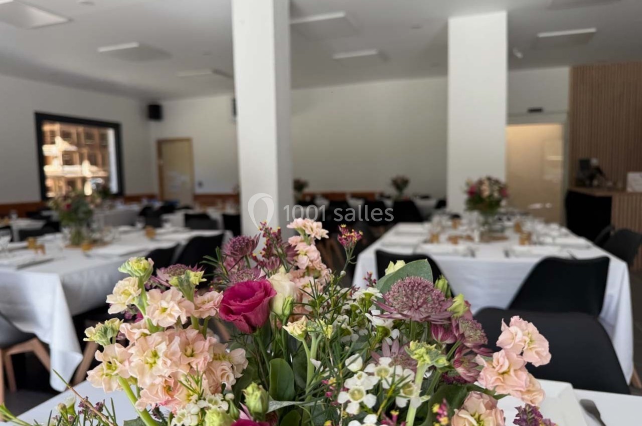 Salle de réception lumineuse avec tables dressées, ornées de bouquets de fleurs colorées au premier plan.