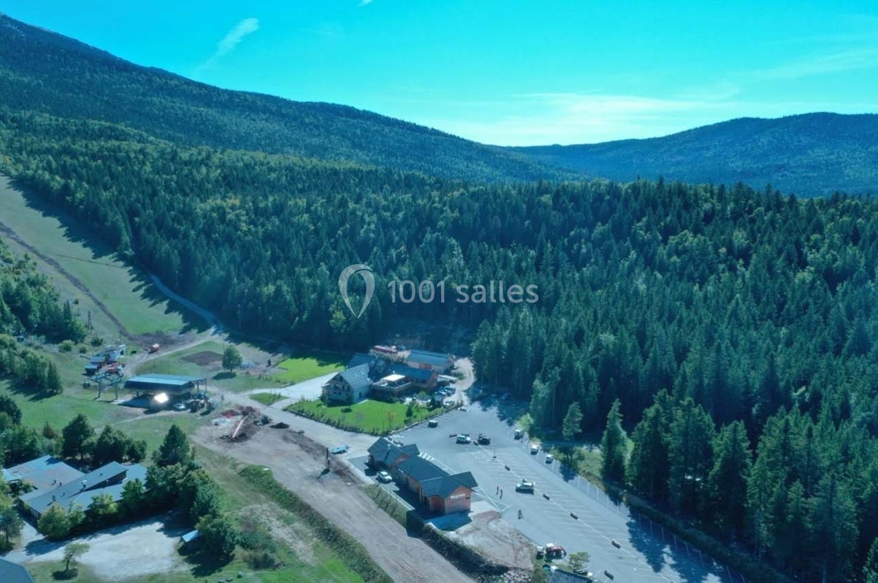 Vue aérienne d'une station de montagne entourée de forêts et de collines sous un ciel bleu dégagé.