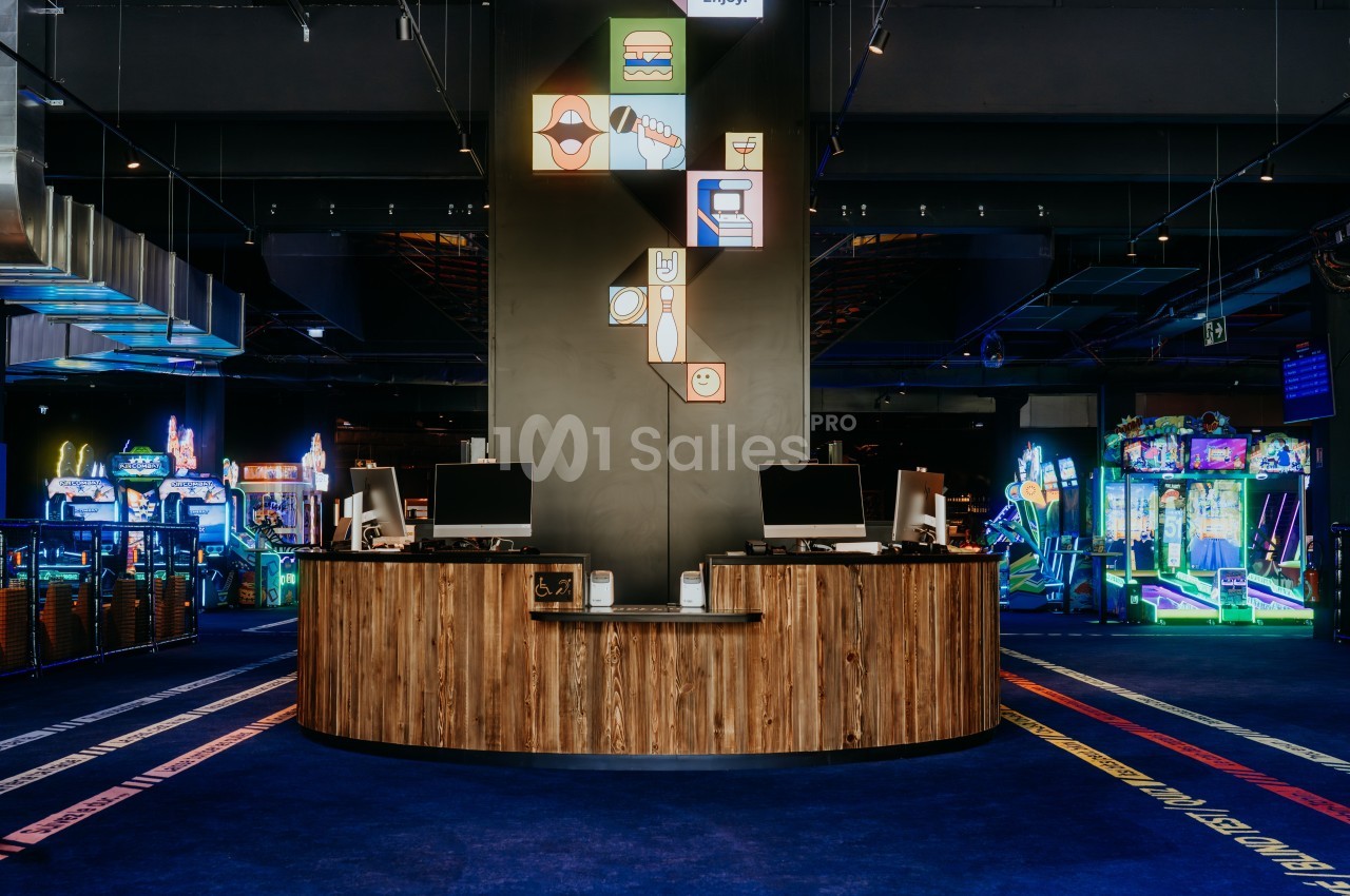 Comptoir en bois avec deux écrans dans une salle d'arcade colorée et lumineuse.