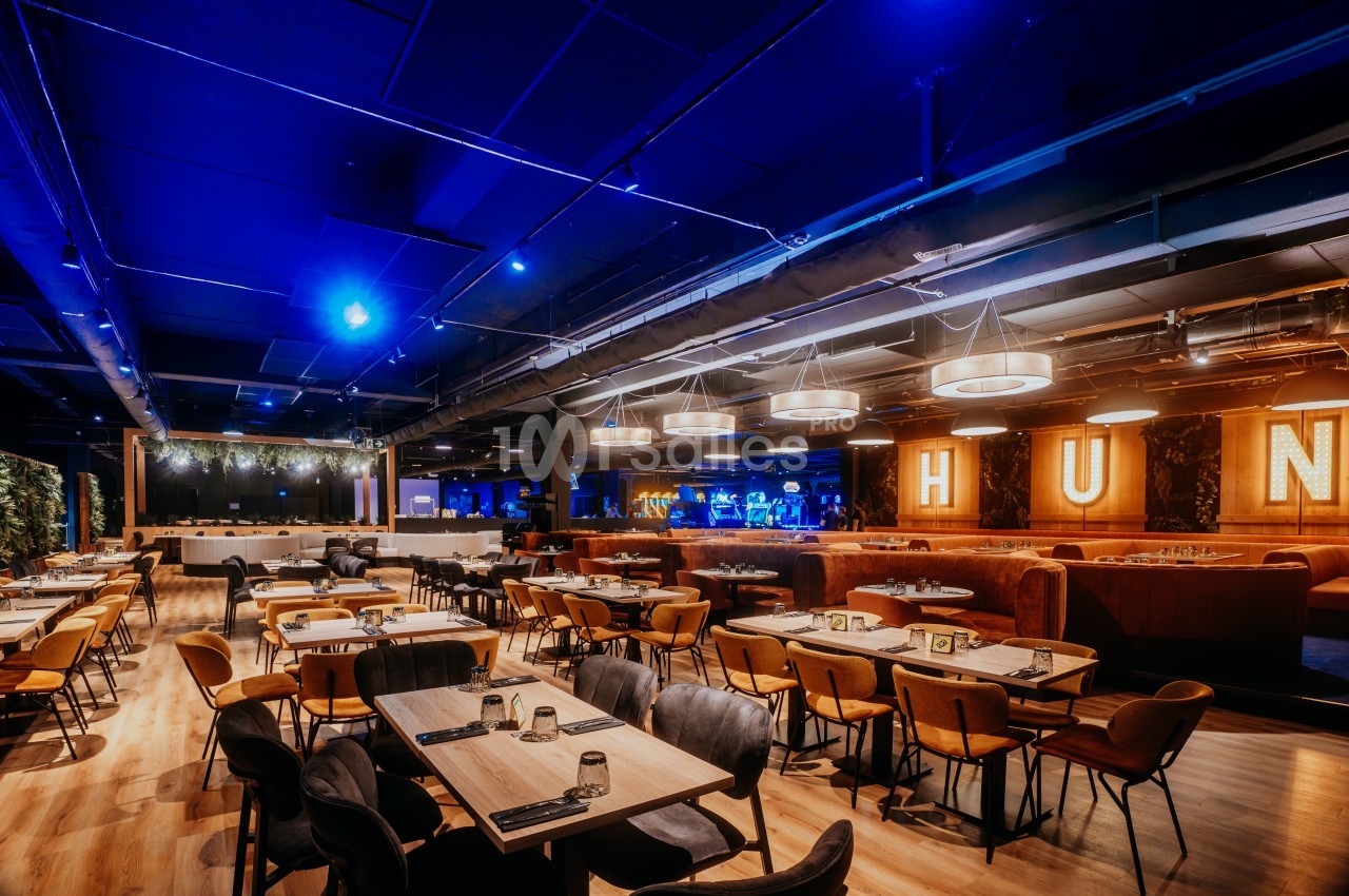 Salle de restaurant moderne avec éclairage tamisé, tables en bois, chaises rembourrées et décorations lumineuses.