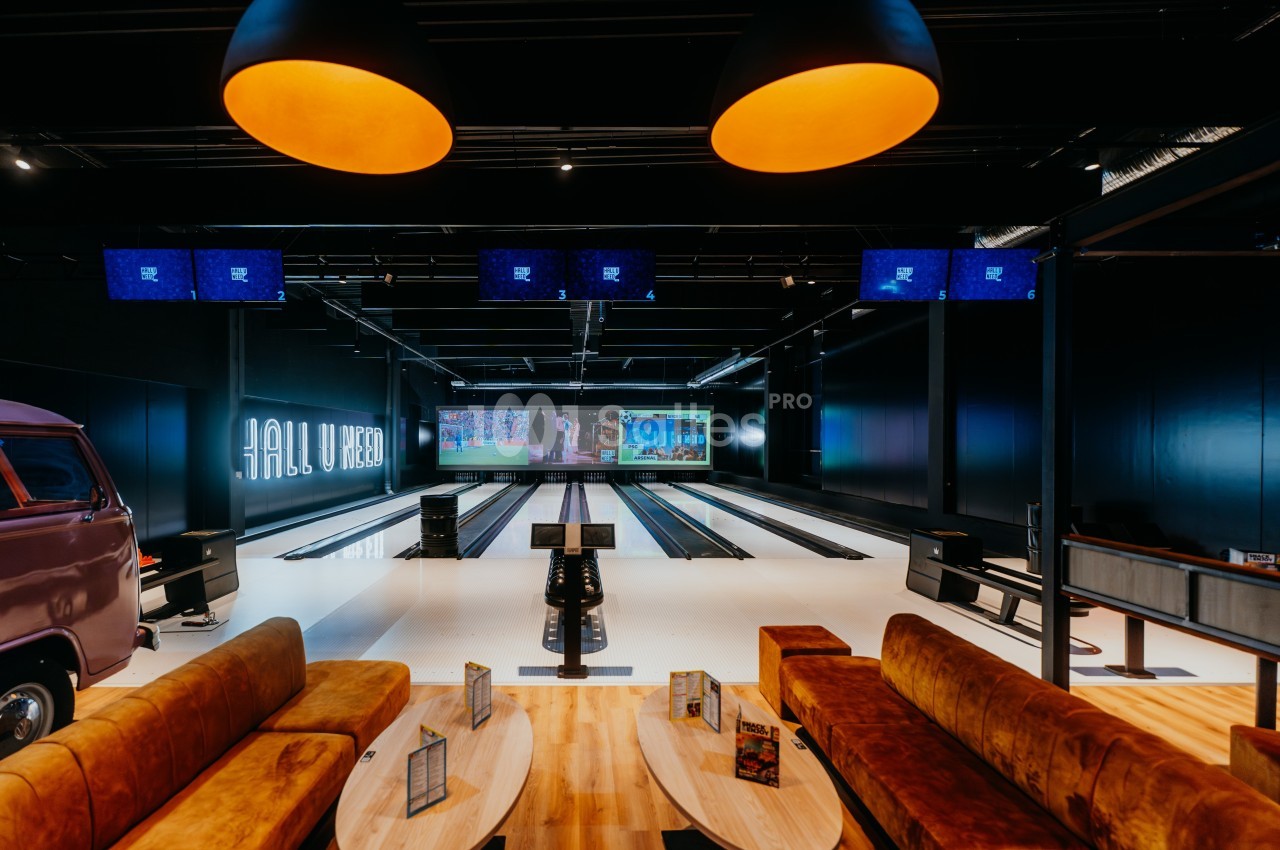 Salle de bowling moderne avec pistes alignées, écrans suspendus et espaces de détente avec canapés et tables.
