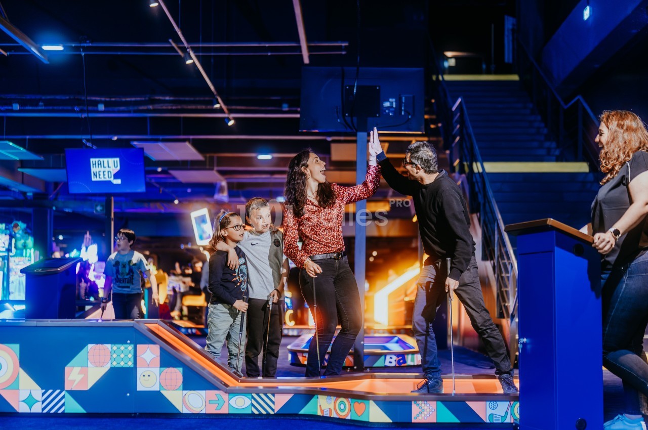 Des adultes et des enfants célèbrent un moment de victoire dans un espace de loisirs lumineux et coloré.