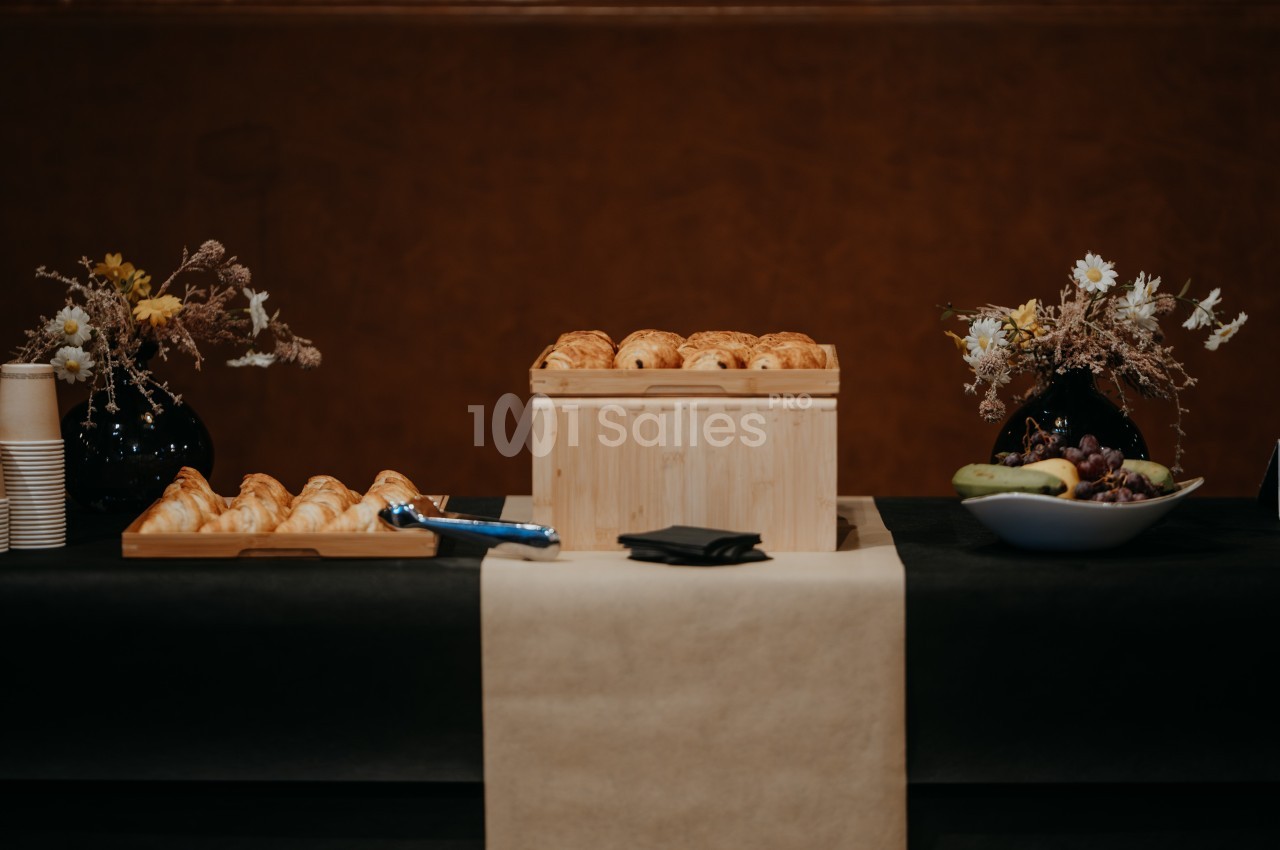 Table avec viennoiseries, fruits, fleurs séchées et gobelets, disposés pour un buffet ou une réception.