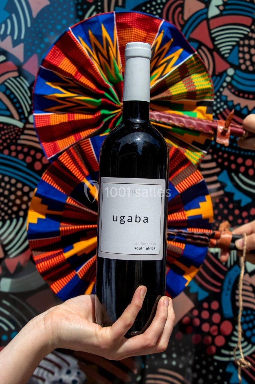 Bouteille de vin rouge tenue devant un éventail coloré et un fond à motifs géométriques vibrants.