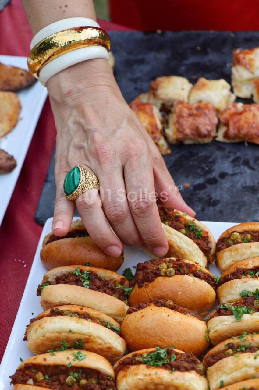 Main prenant un petit sandwich garni de viande hachée et de légumes sur un plateau lors d'un buffet.