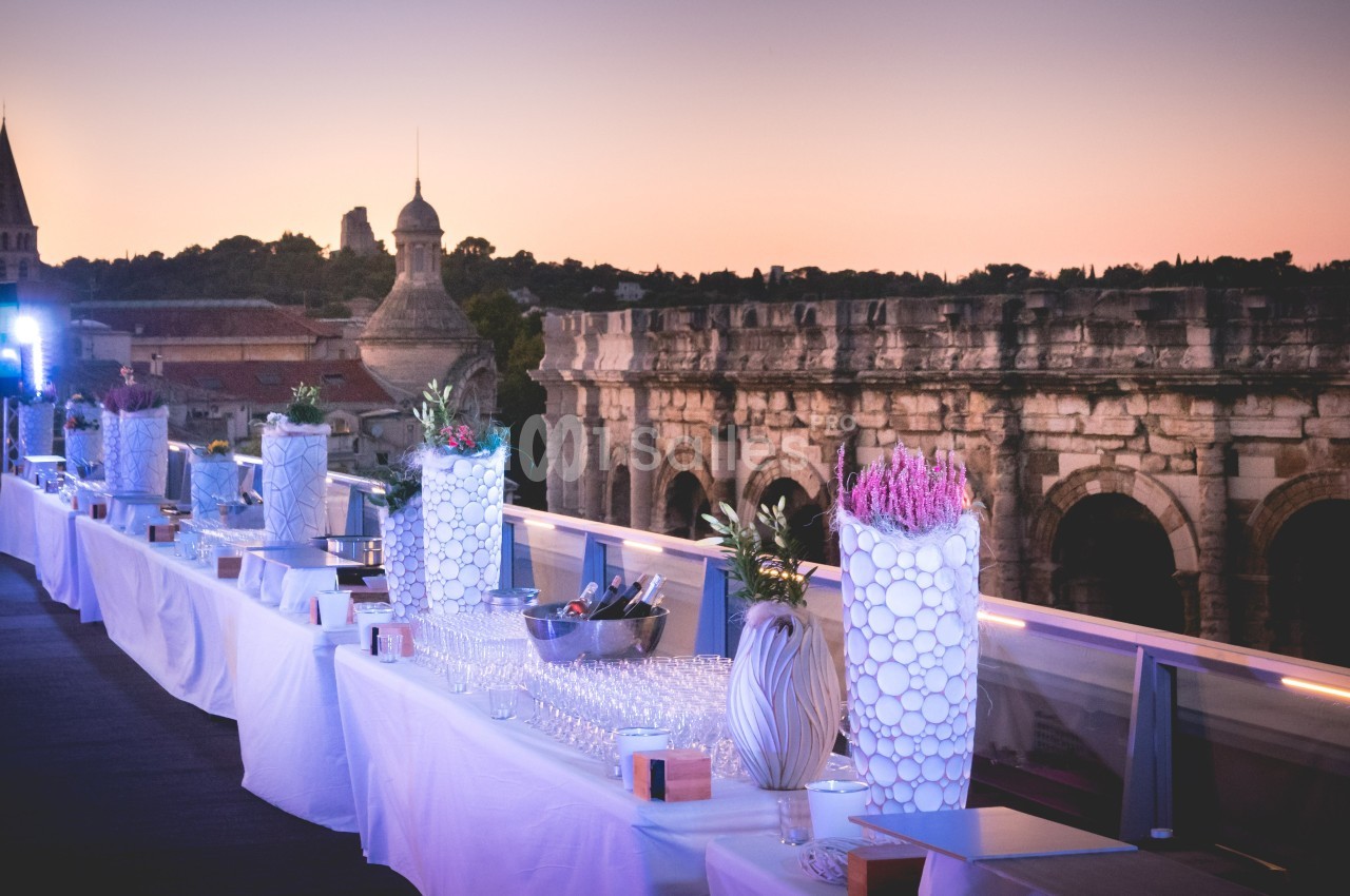 Terrasse aménagée pour un événement avec tables dressées, vue sur des monuments historiques au coucher du soleil.