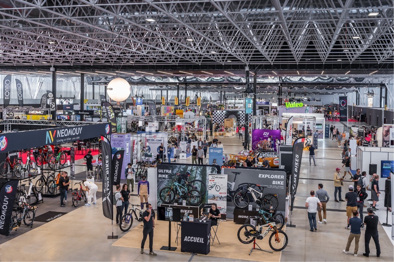 Vue d'ensemble d'un salon professionnel dédié au cyclisme avec stands, vélos exposés et visiteurs.