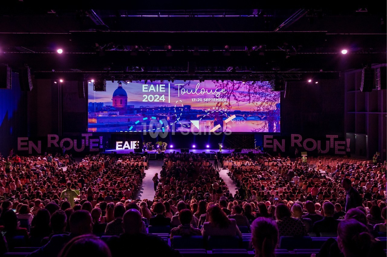 Salle de conférence bondée avec une scène illuminée affichant ’EAIE 2024 Toulouse, 17-20 septembre’.