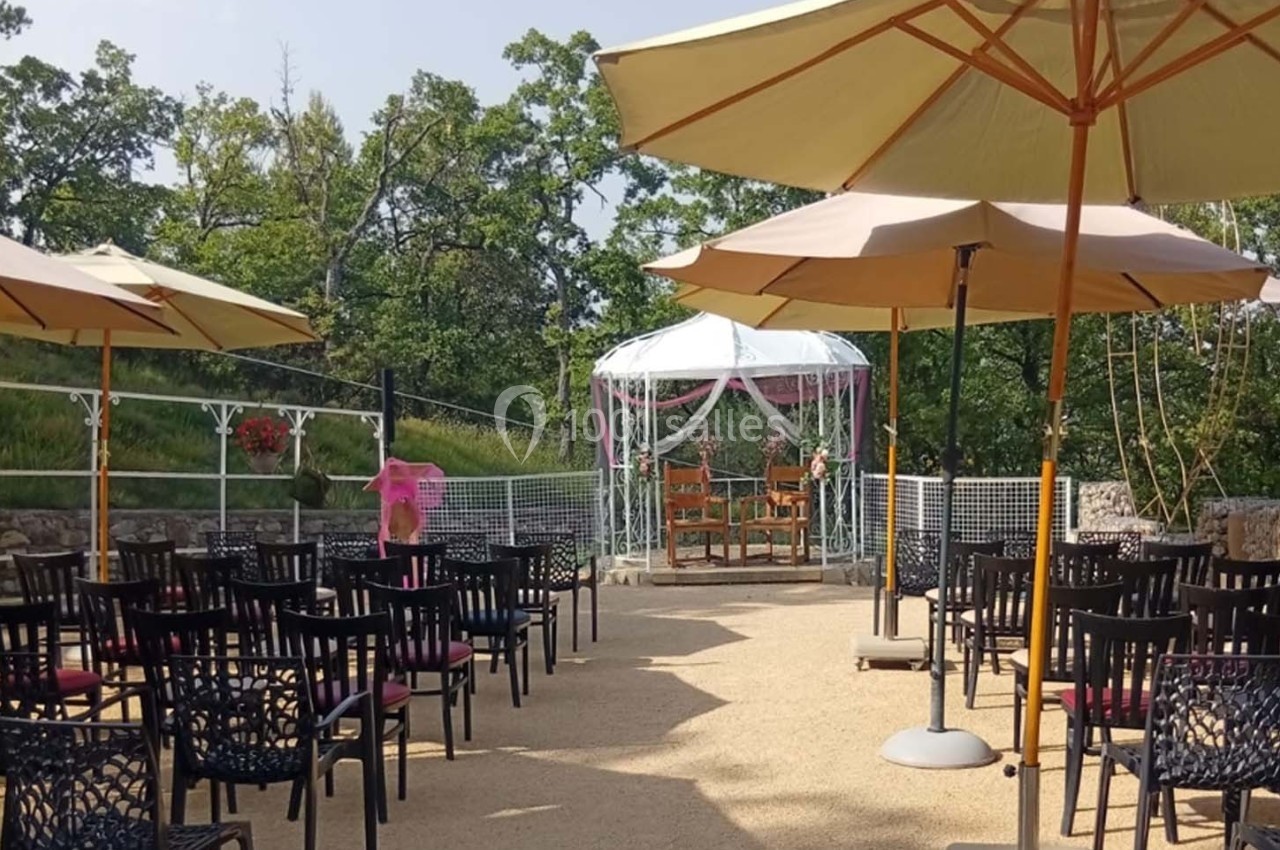 Chaises disposées en rangées sous des parasols face à une arche décorée pour une cérémonie en extérieur.