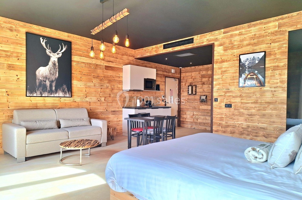 Chambre moderne en bois avec lit, canapé, coin cuisine, table à manger et décoration murale de cerfs.