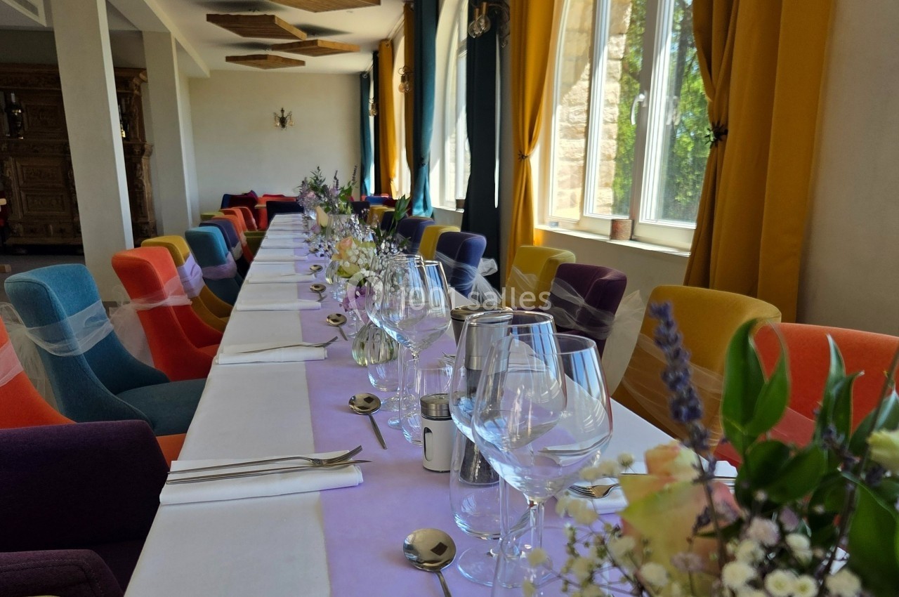 Table dressée pour un repas, décorée de fleurs et entourée de chaises colorées dans une salle lumineuse.