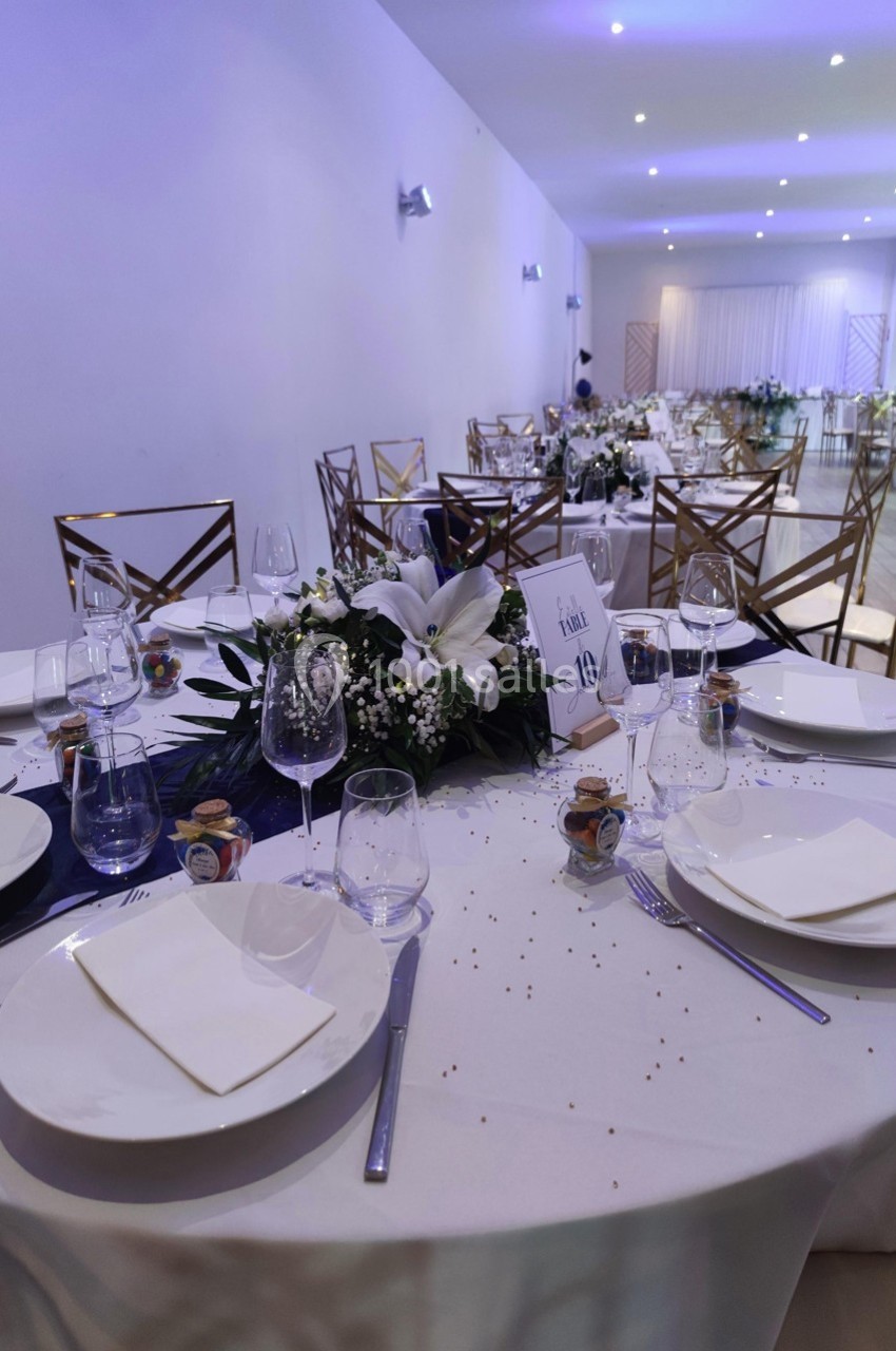 Tables élégamment dressées avec nappes blanches, vaisselle raffinée et centre de table floral dans une salle de réception.