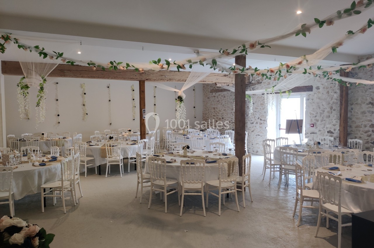 Salle de réception décorée avec des tables rondes dressées, des chaises blanches et des guirlandes végétales suspendues.