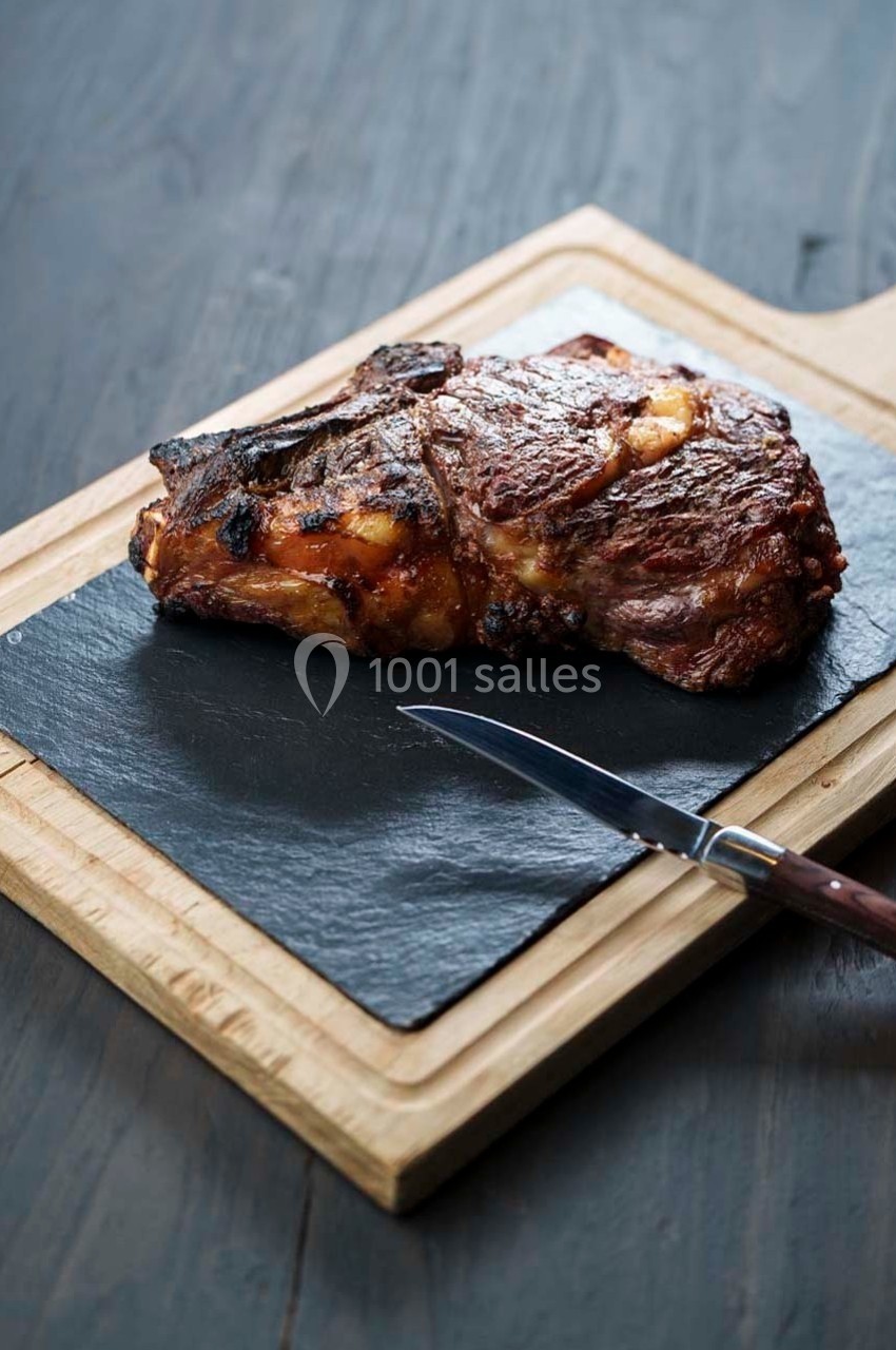 Côte de bœuf grillée servie sur une planche en ardoise avec un couteau en bois.