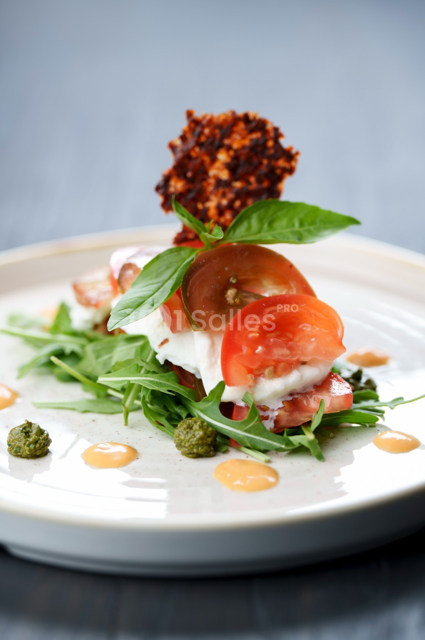Assiette garnie de roquette, tomates, mozzarella, pesto et chips croustillante, présentée de façon élégante.
