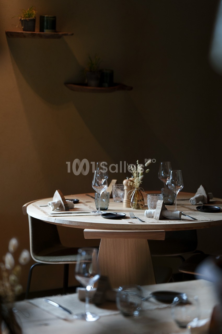 Table ronde en bois dressée avec verres, couverts et décorations minimalistes dans une ambiance tamisée.