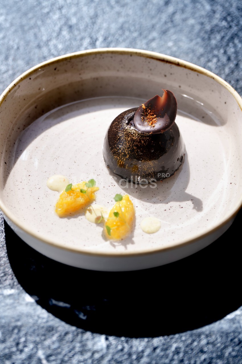 Dessert chocolaté avec garniture en coque brillante, accompagné de segments d'agrumes et de touches de sauce.