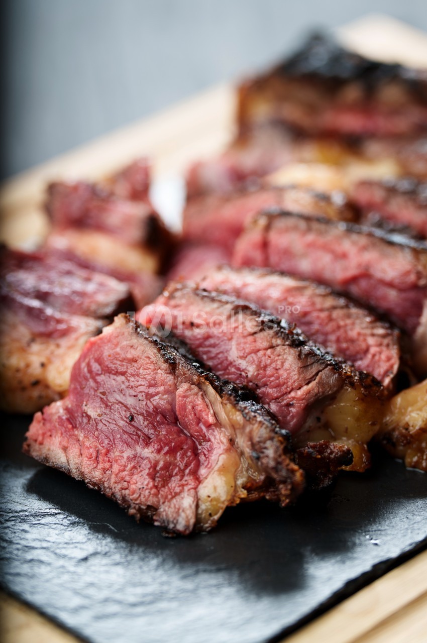 Tranches de steak grillé, juteuses et saignantes, servies sur une ardoise noire.