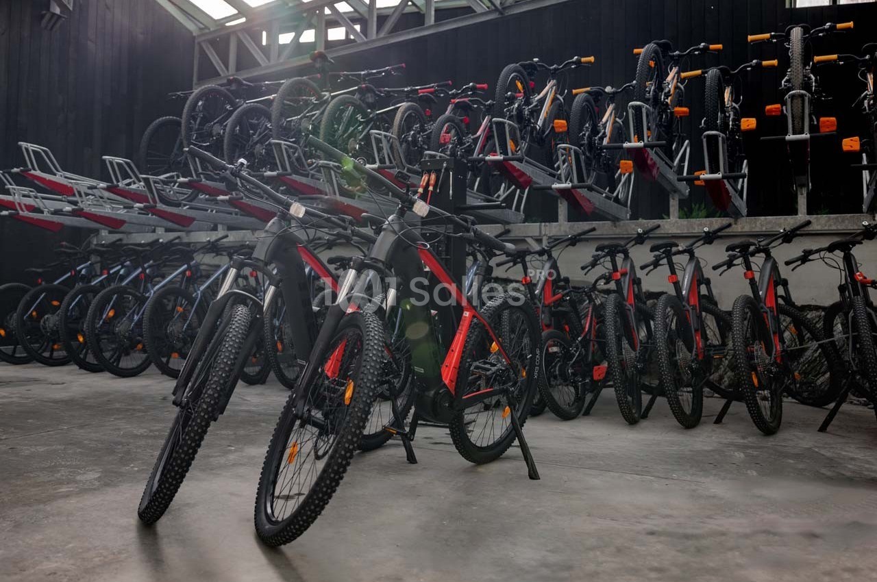 Rangée de vélos électriques noirs et rouges alignés dans un entrepôt avec des supports de rangement en arrière-plan.