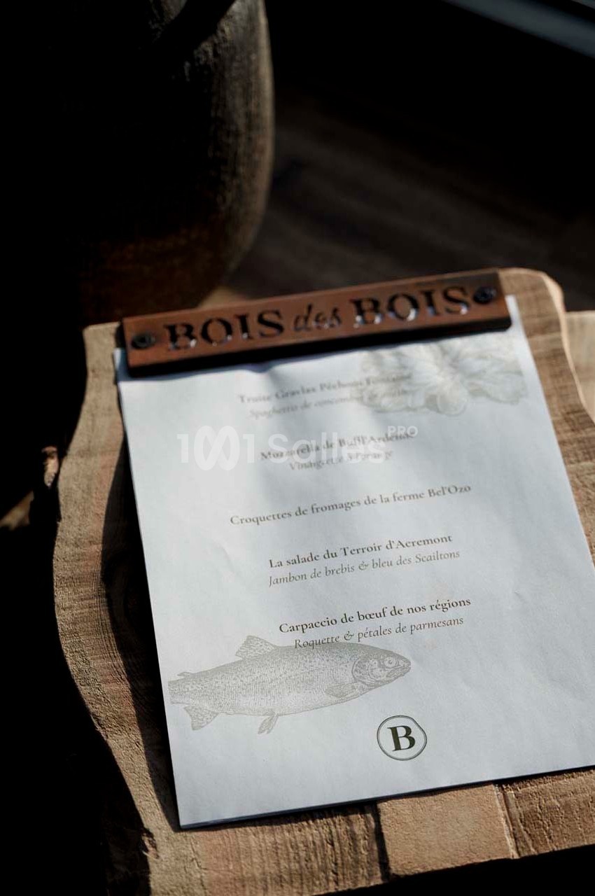 Carte de menu posée sur une planche en bois, éclairée par une lumière naturelle, avec des plats inscrits en texte.