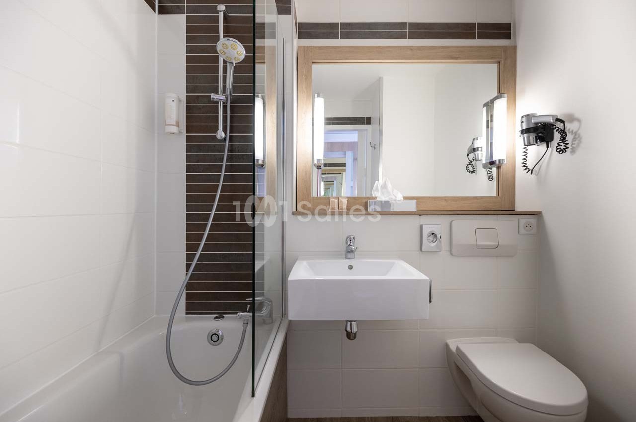 Salle de bain moderne avec baignoire, lavabo, miroir encadré en bois, toilettes et éclairage mural.