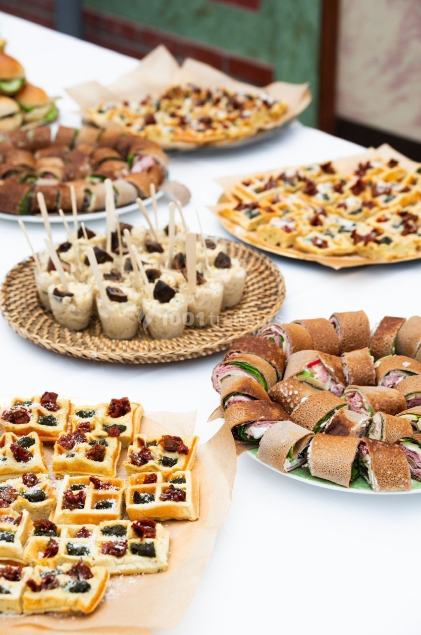 Assortiment de plats variés comprenant gaufres salées, roulés, verrines et autres amuse-bouches sur une table.