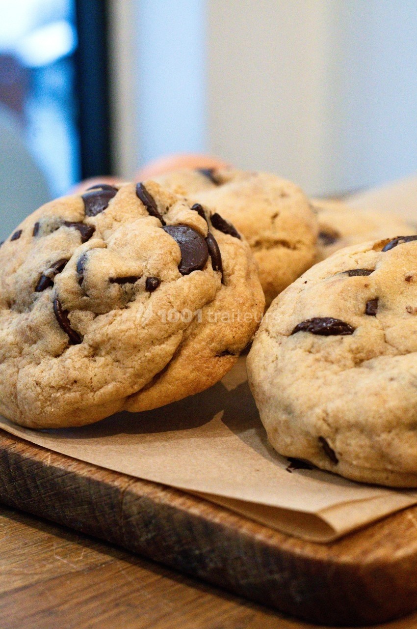 Cookies aux pépites de chocolat posés sur une planche en bois, avec un fond flou.