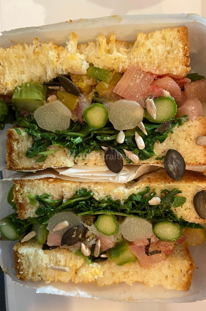 Sandwich garni de légumes frais, graines, asperges et verdure, présenté en coupe sur du pain moelleux.