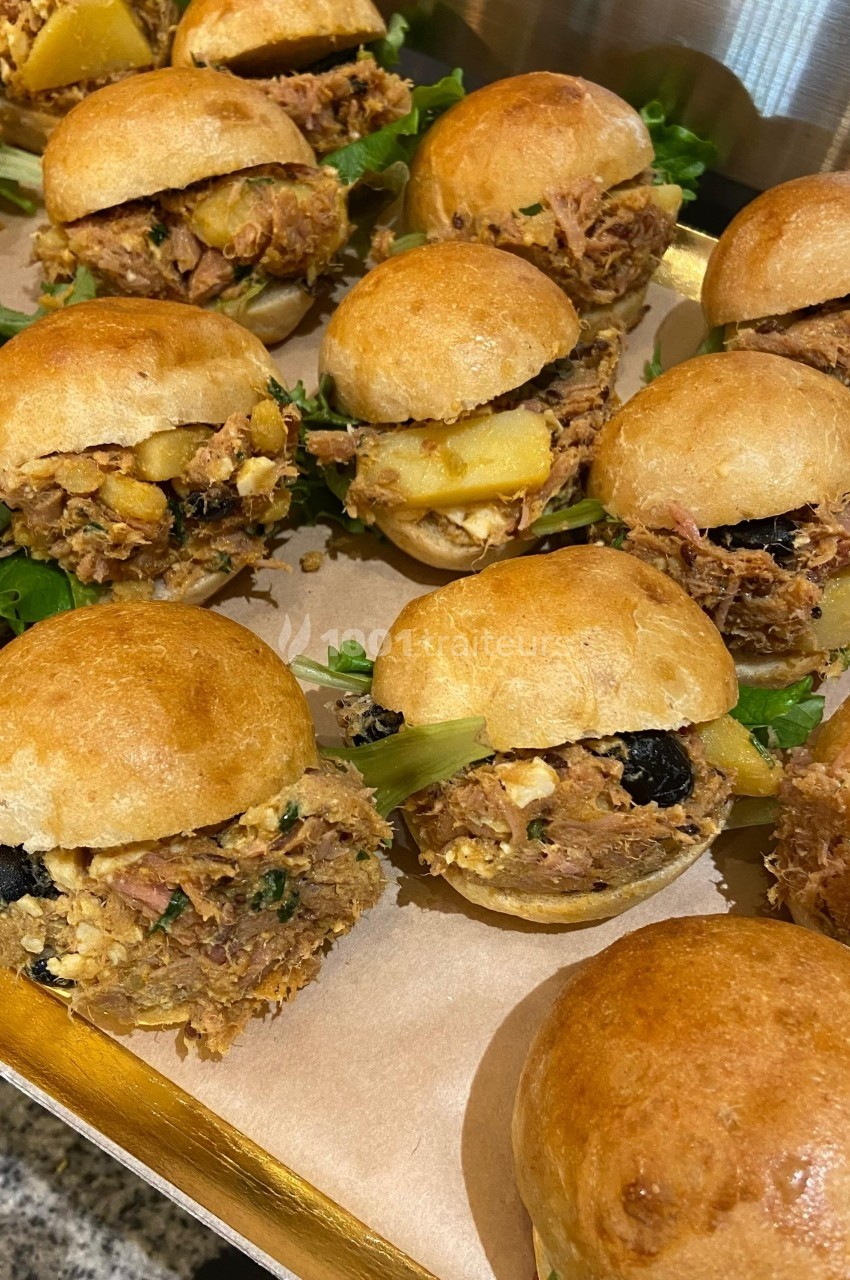 Petits burgers garnis de viande effilochée, fromage, olives et légumes, présentés sur un plateau en bois.