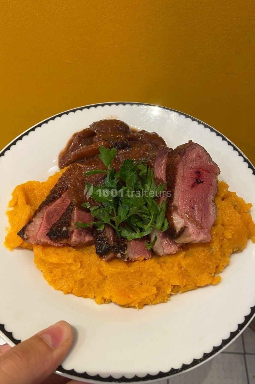 Assiette de magret de canard tranché sur purée de patates douces, garni de persil et accompagné d'une sauce.