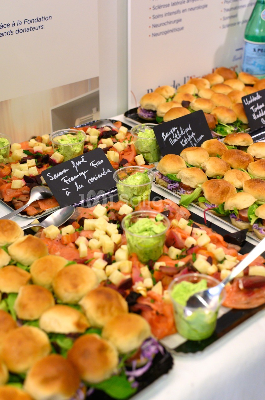 Plateaux de mini-sandwichs variés avec garnitures, accompagnés de verrines de sauce verte et étiquettes descriptives.